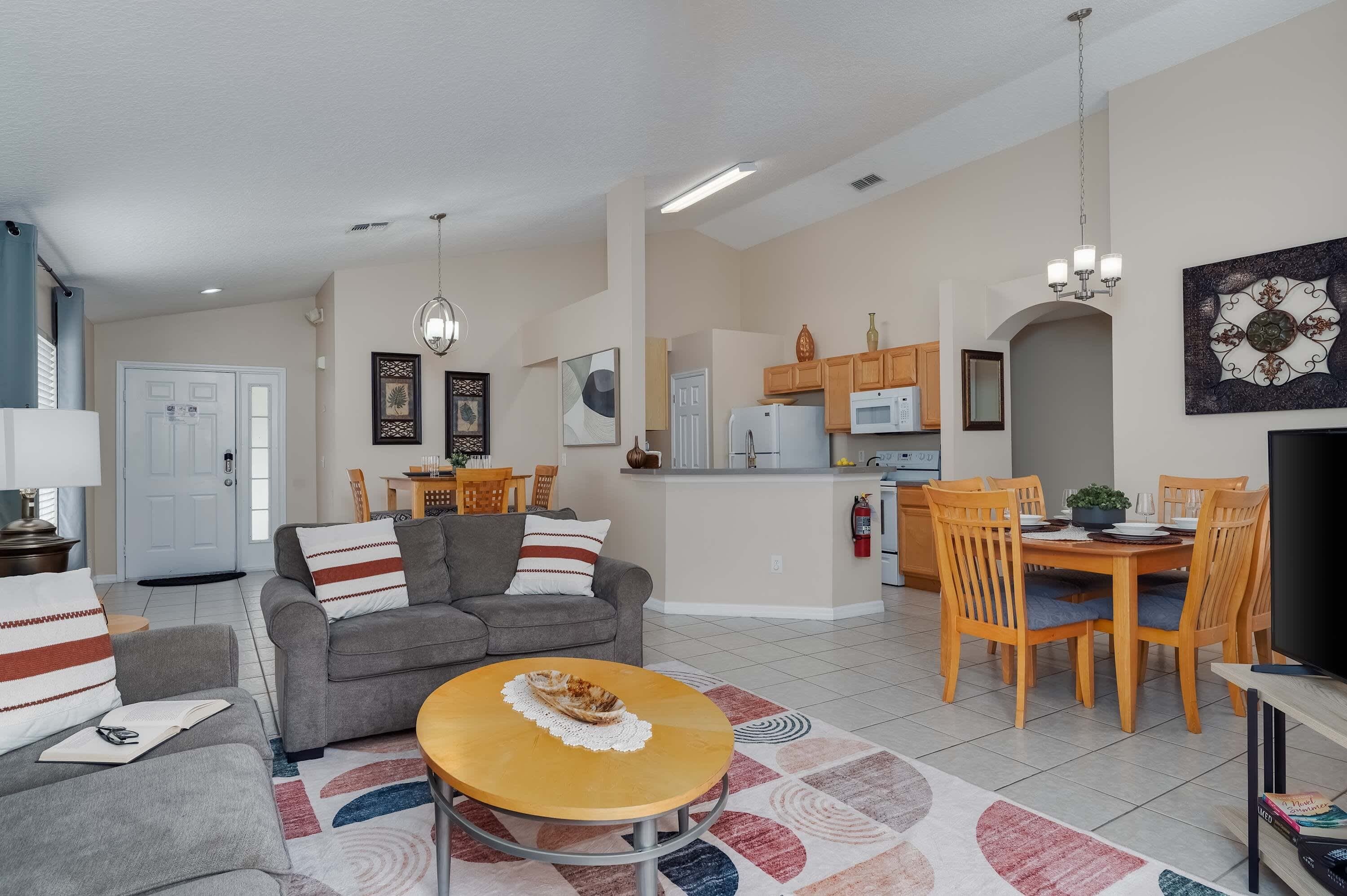 A modern living room with a grey sofa, a wooden coffee table, and a dining area with wooden chairs and a table.