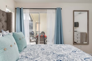 Ein Schlafzimmer mit Bett, einem Fenster mit Vorhängen, einem Essbereich mit Stühlen und Tisch sowie einem Spiegel an der Wand.