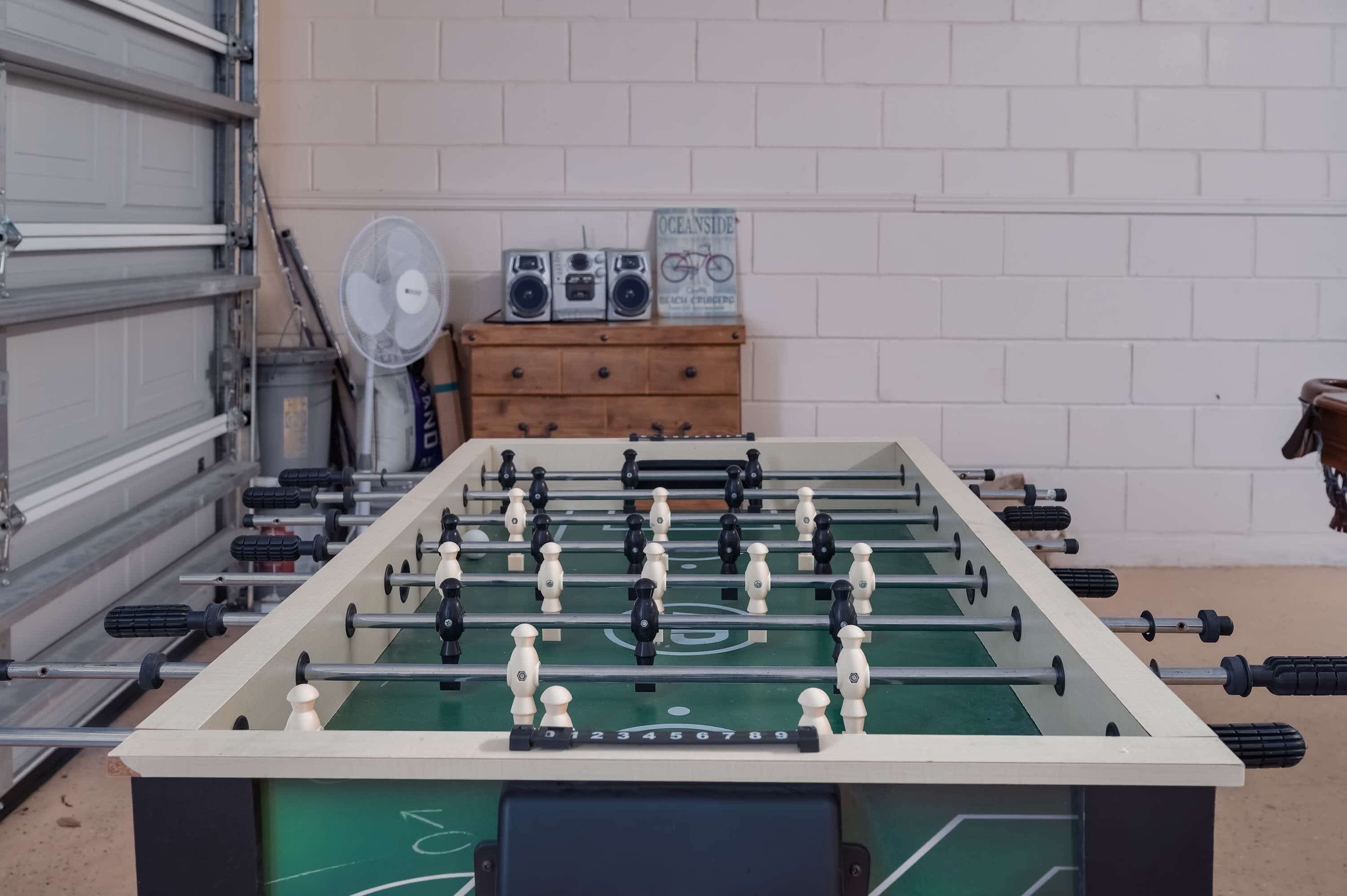 A foosball table with a scoreboard, a fan, and a radio set against a brick wall.