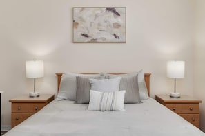 Ein Schlafzimmer mit einem Bett, zwei Nachttischen und einem an der Wand hängenden abstrakten Gemälde.