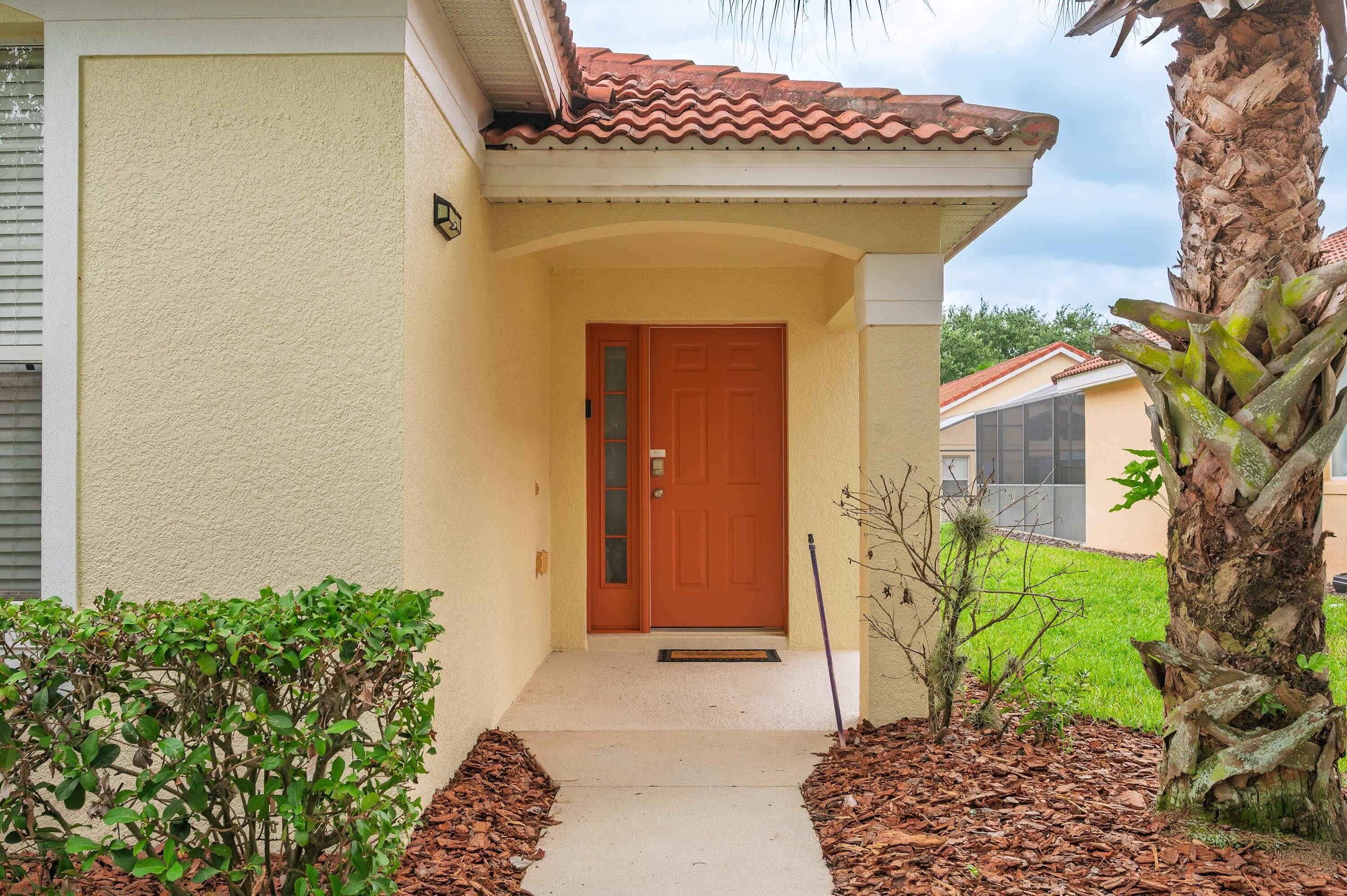 A residential building with a red door, a small porch, and a palm tree.