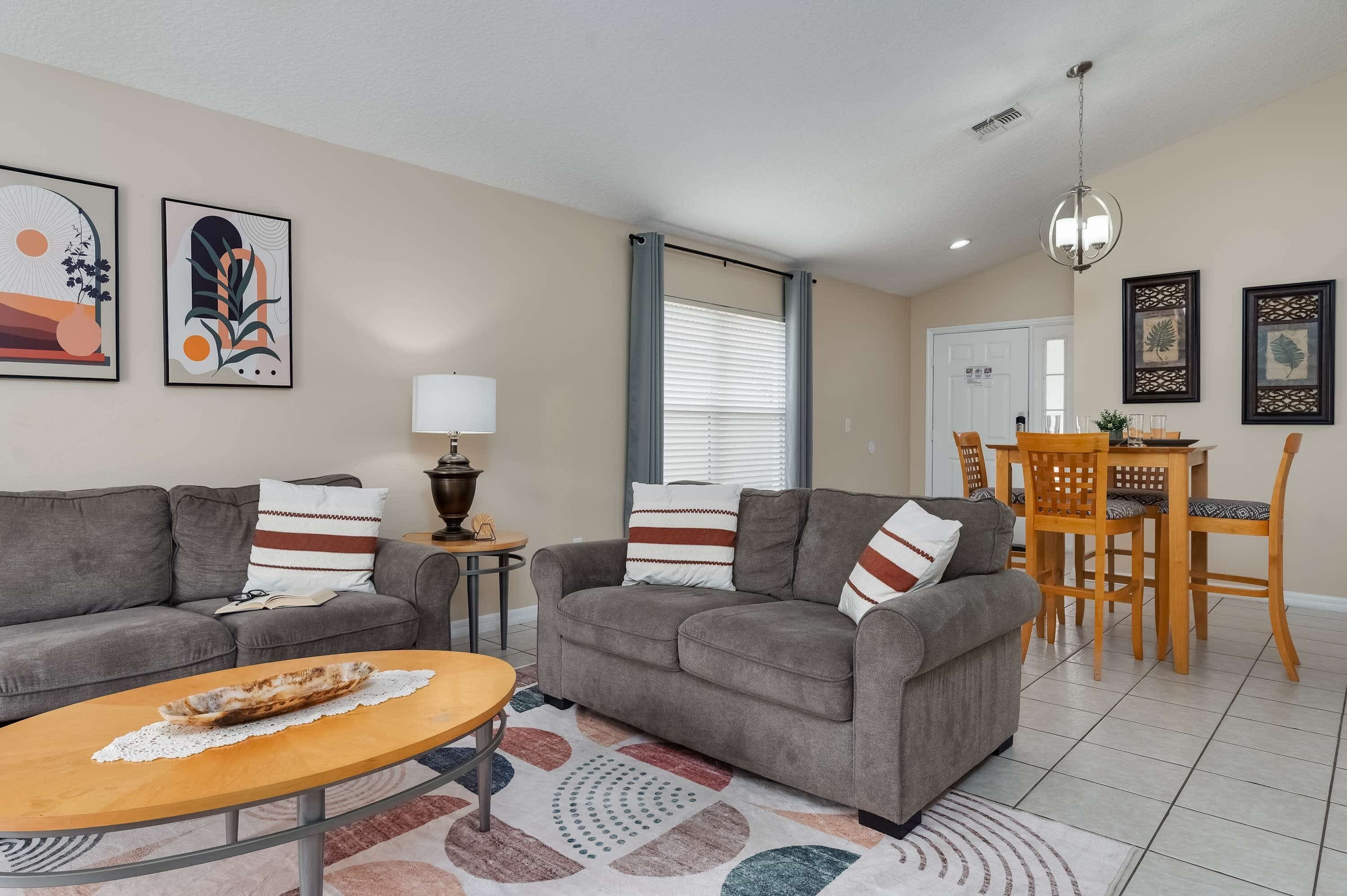 A living room with a sofa, a coffee table, a lamp, and a dining area with a table and chairs.