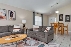 Ein Wohnzimmer mit Sofa, Couchtisch, Lampe und einem Essbereich mit Tisch und Stühlen.