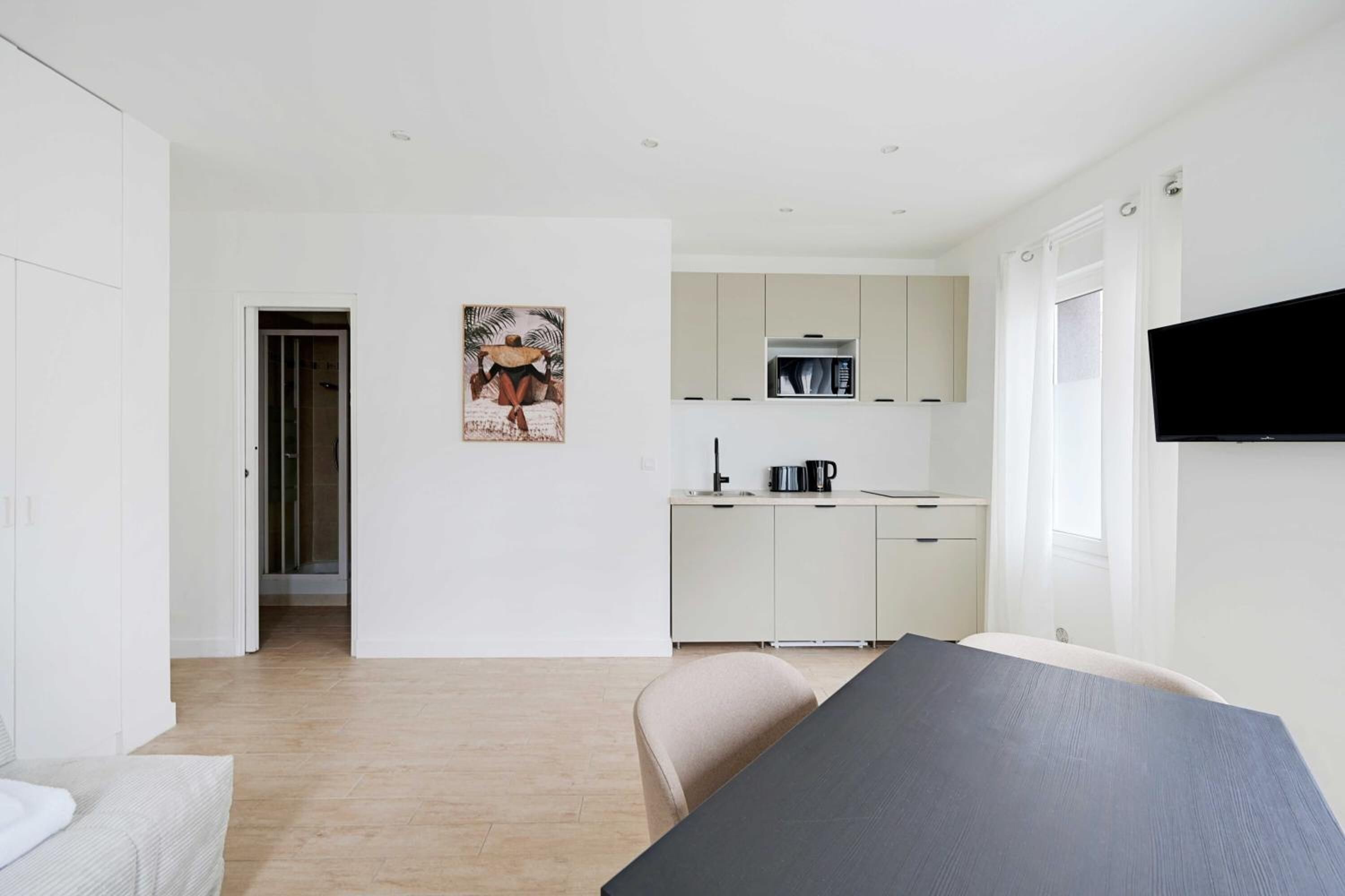 Un espace de vie moderne et minimaliste comprenant un coin repas, une kitchenette et un téléviseur à écran plat fixé au mur.