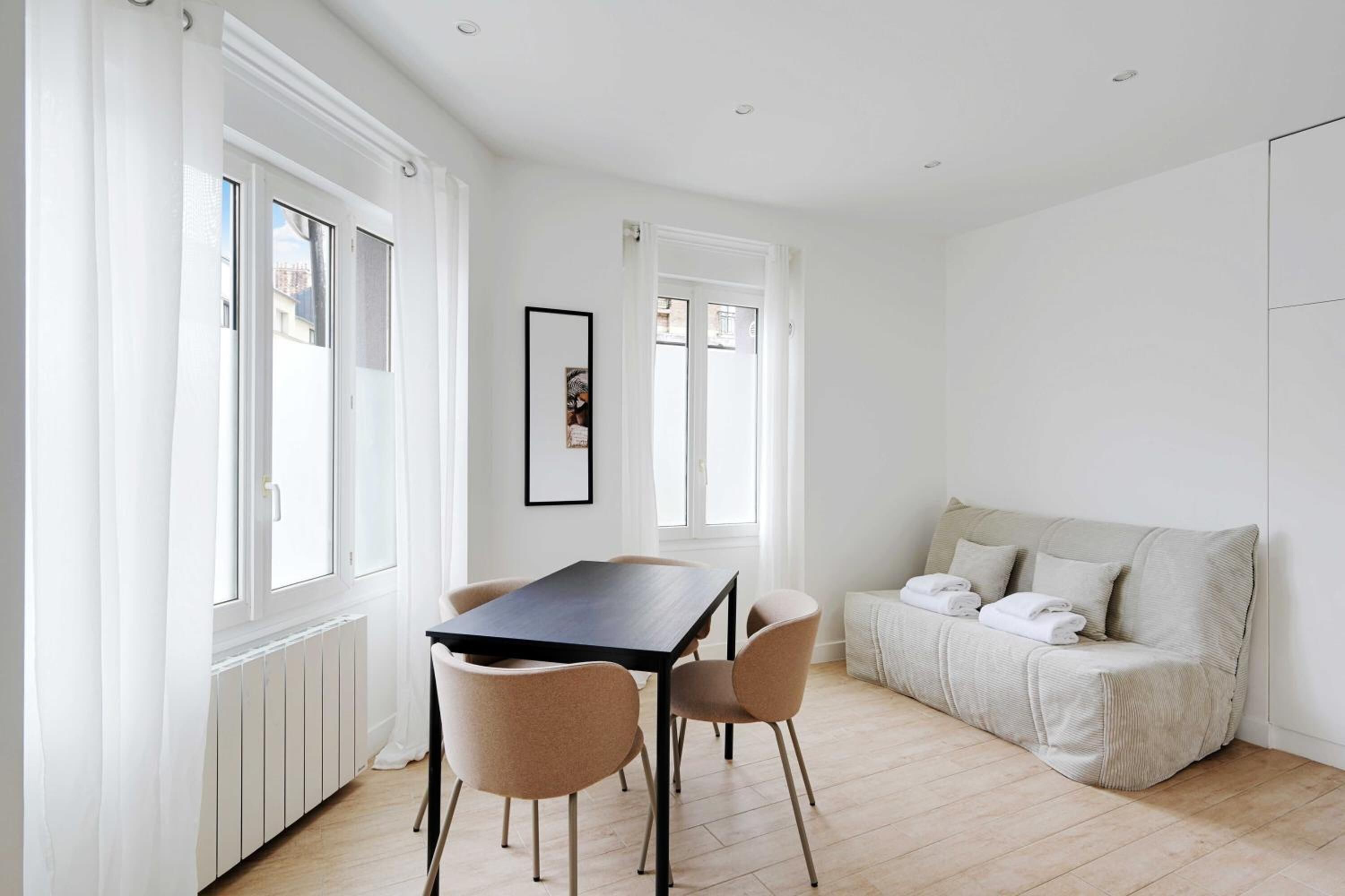 Une pièce moderne et bien éclairée, avec une table à manger, des chaises, un canapé et un tableau encadré au mur.