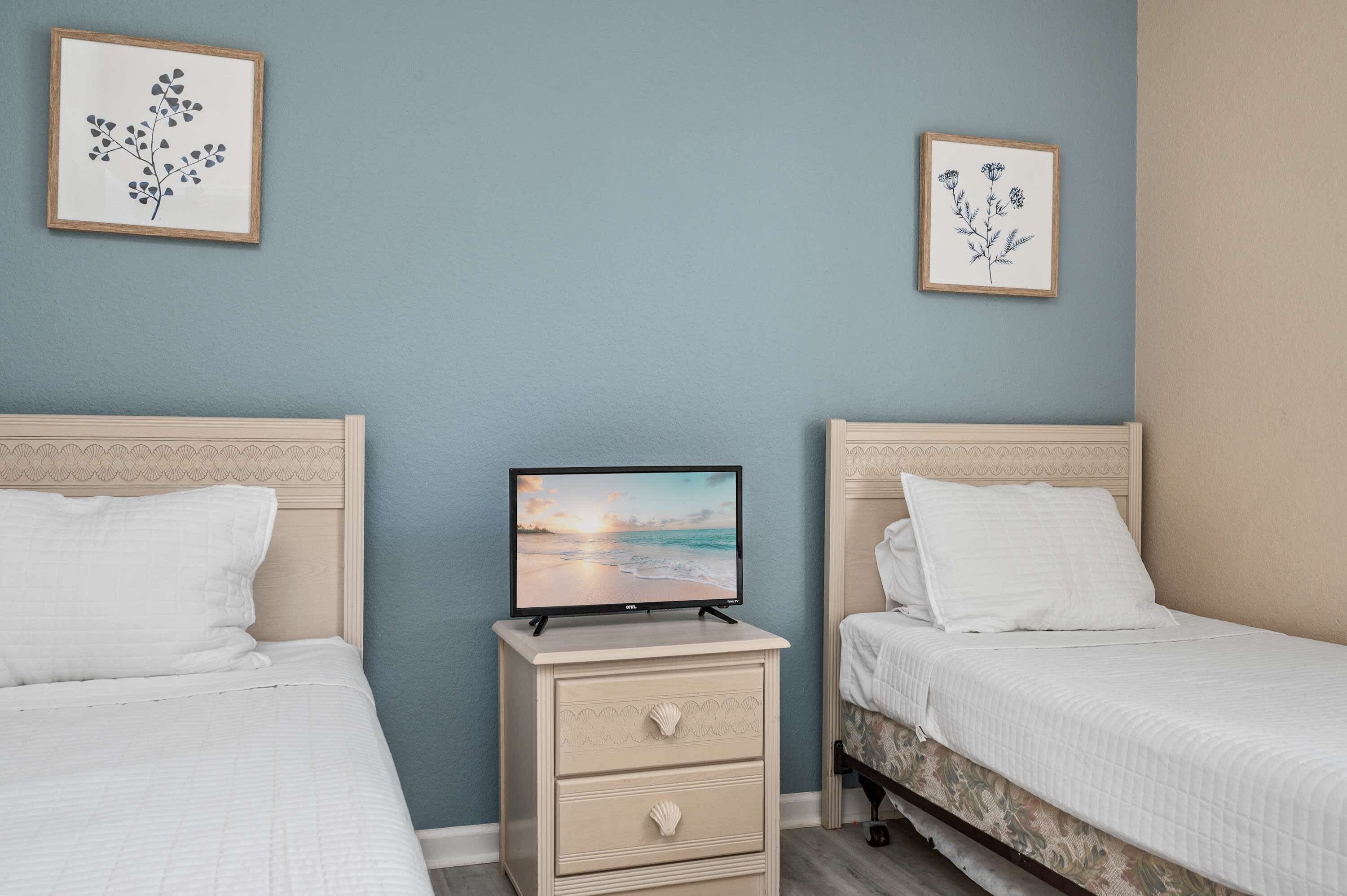 A bedroom with two beds, a nightstand with a TV, and wall art.