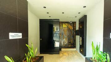 A hallway with dark tiled walls, a sign prohibiting sitting in the gardens, and potted plants at the end.