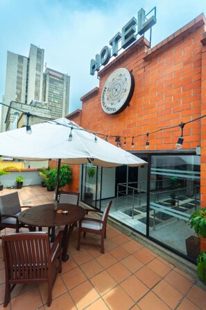 A hotel with a brick facade, a signboard, a round emblem, and outdoor seating with umbrellas. - Mandala Medellin Botero By Gyc Hotels (Medellín)