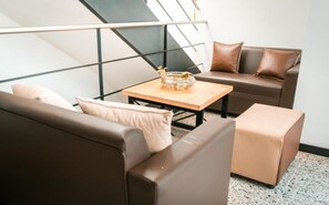 A modern living room with a sofa, ottoman, and coffee table, featuring a geometric wall design and a glass bowl on the table. - Mandala Medellin Botero By Gyc Hotels (Medellín)