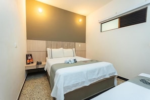 A hotel room with a bed, a bedside table, a wall-mounted light, and a window with blinds. - Mandala Medellin Botero By Gyc Hotels (Medellín)