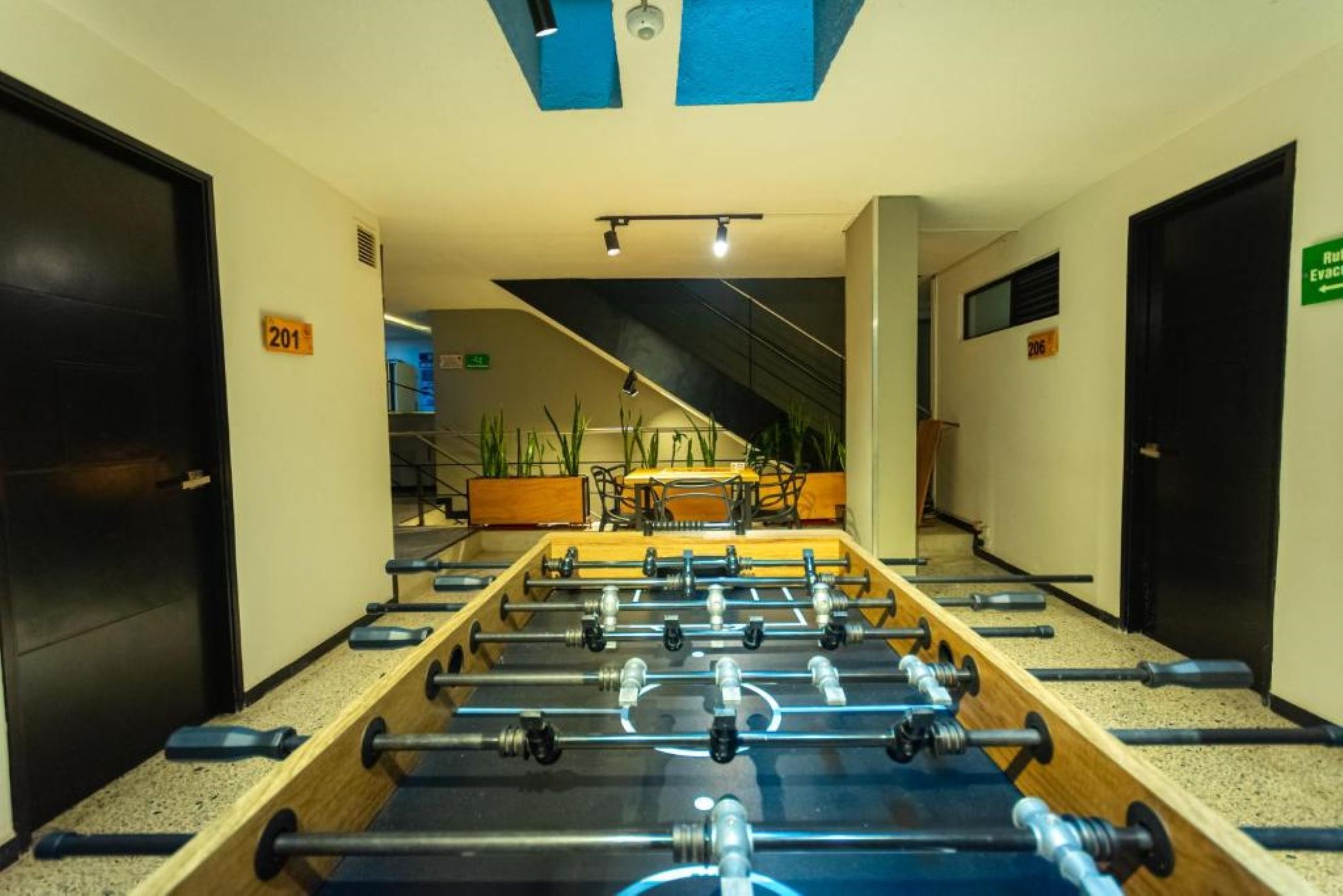 A corridor with a foosball table, doors numbered 201 and 206, and a green exit sign.