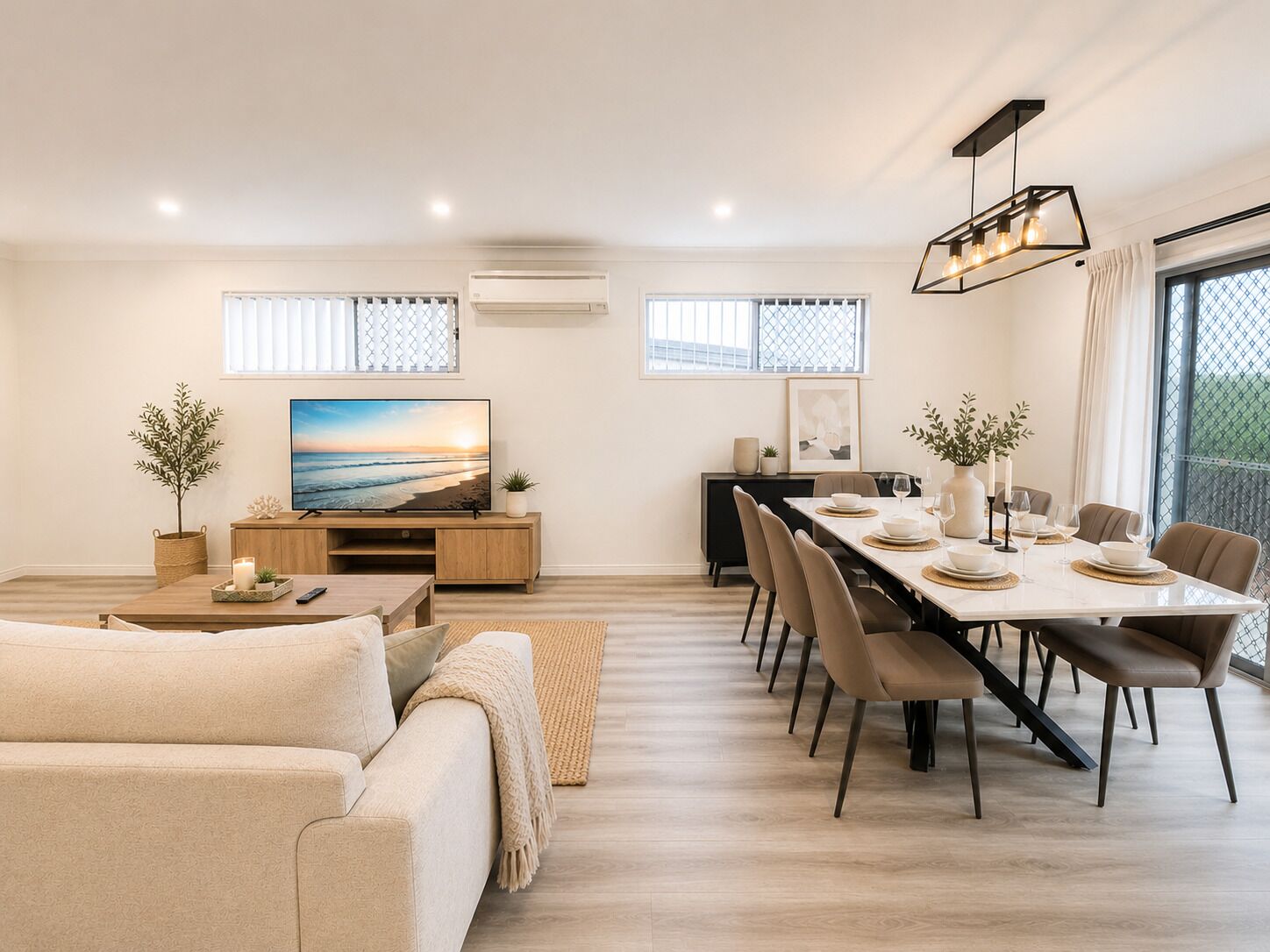 Ein modernes Wohnzimmer mit Sofa, Fernseher, Essbereich und einem Balkon mit Blick.