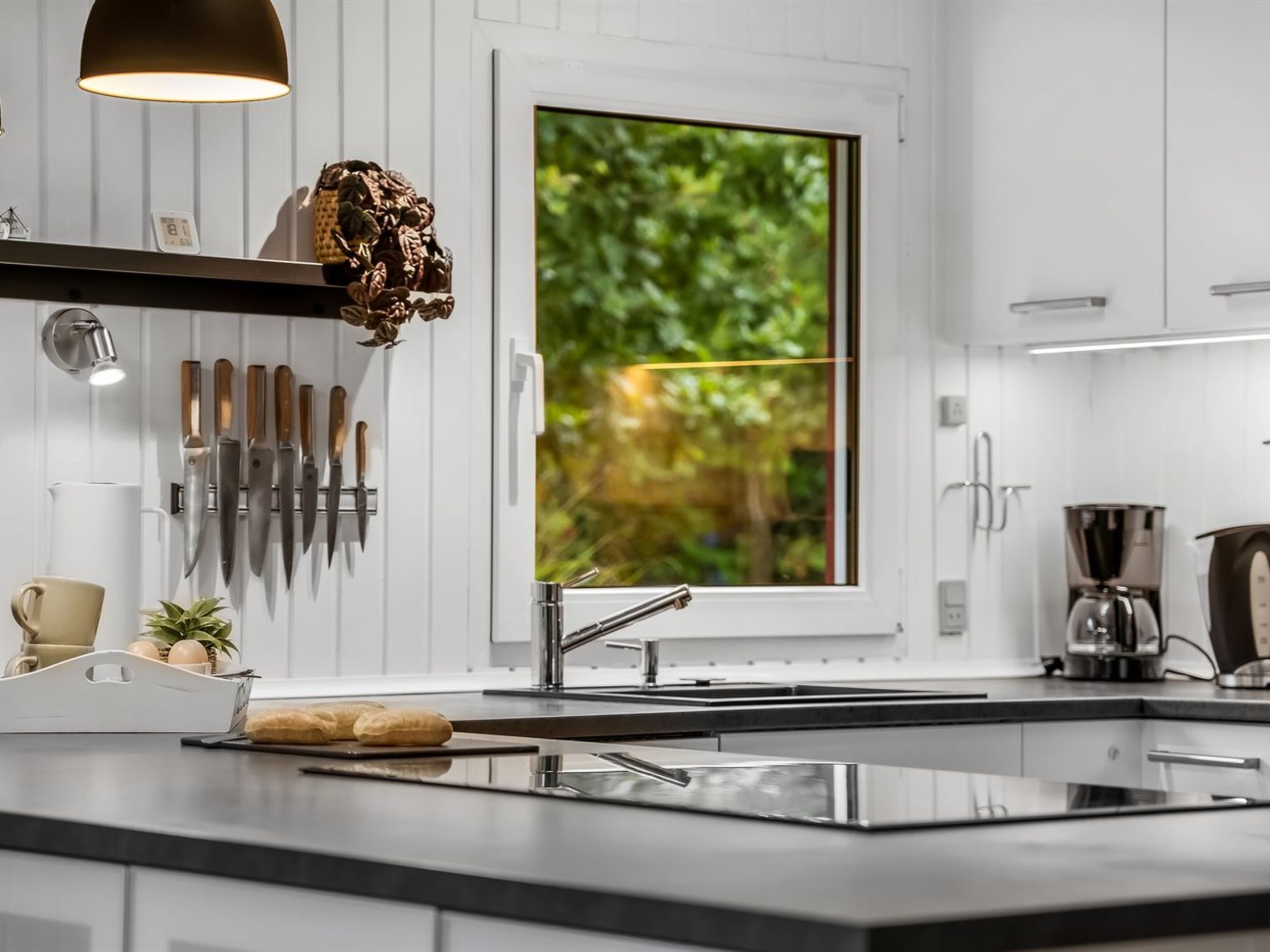 A modern kitchen with a large window, a sink, and a variety of knives.