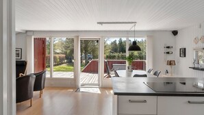 Een moderne keuken met een groot eiland, schuiframen naar een terras en een eetgedeelte met stoelen.
