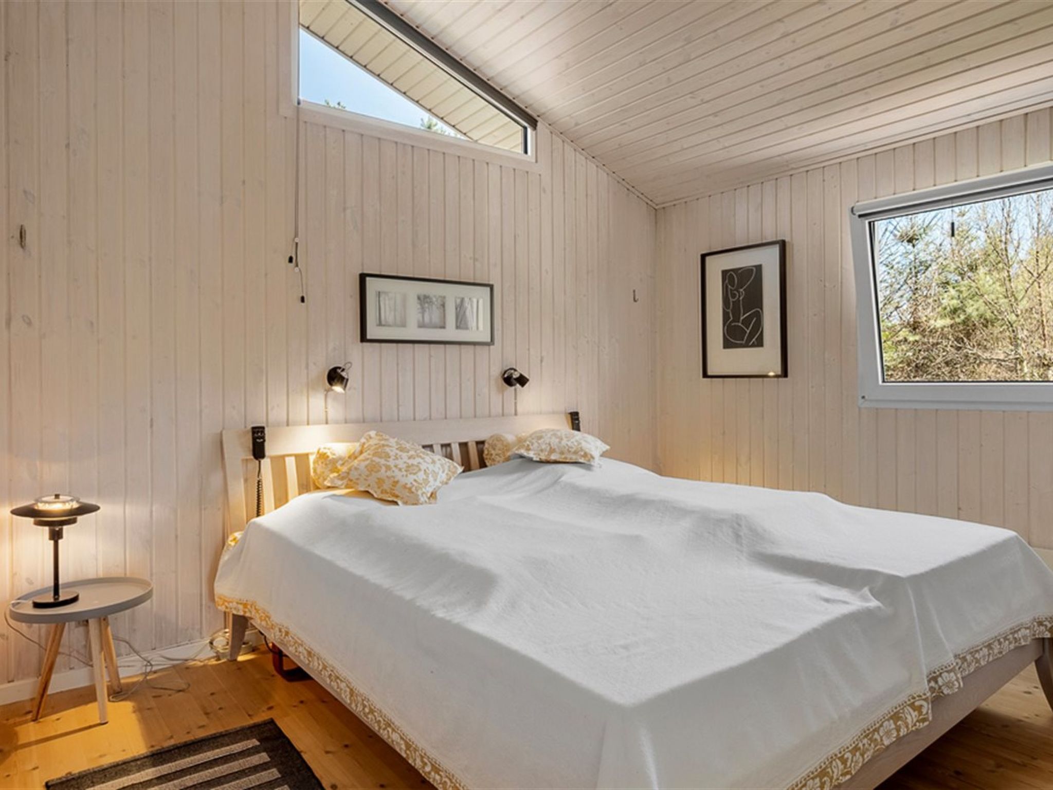 Ein Schlafzimmer mit einem Bett, einem kleinen Tisch, einem Fenster und einem gerahmten Bild an der Wand.