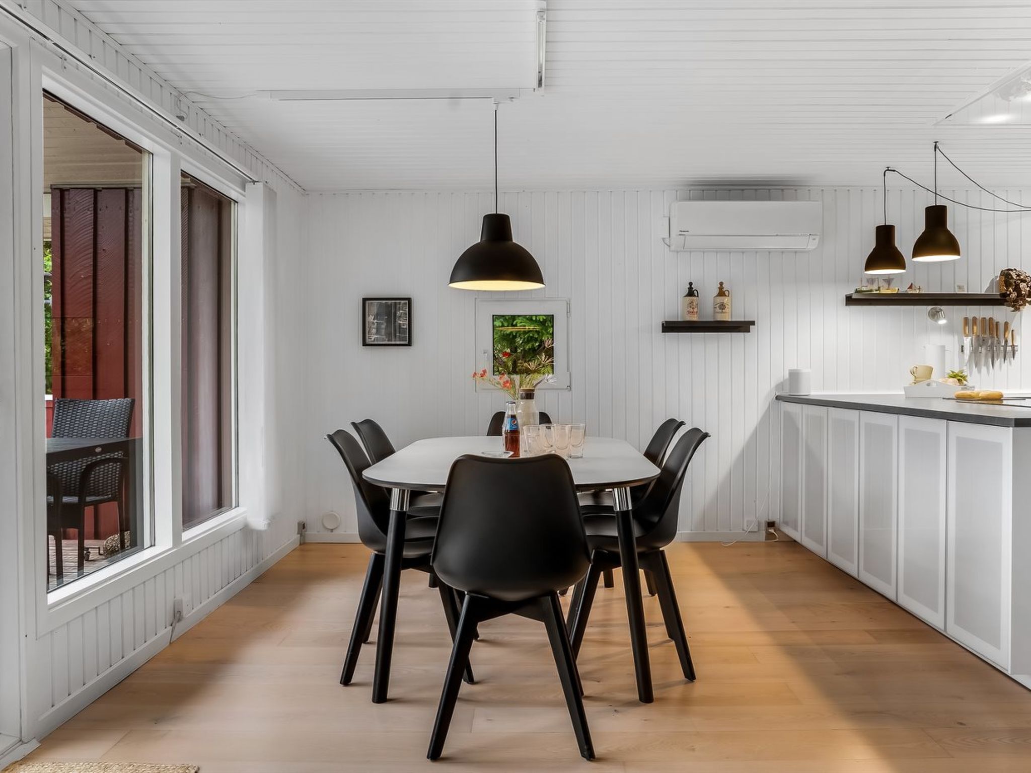 A dining area with a round table, black chairs, pendant lighting, and a view of the outdoors.