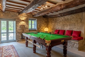 A pool table in a room with stone walls, a wooden ceiling, and a red sofa. - Tenuta Santa Cristina 10, Emma Villas (Gubbio)