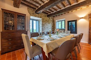 A dining room with a table set for six, stone walls, a wooden cabinet with glass doors, and a framed painting on the wall.