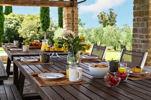 Ein Holzespeisetisch im Freien, gedeckt mit Tellern, Besteck, einer Blumenvase und einer Schale Erdbeeren.