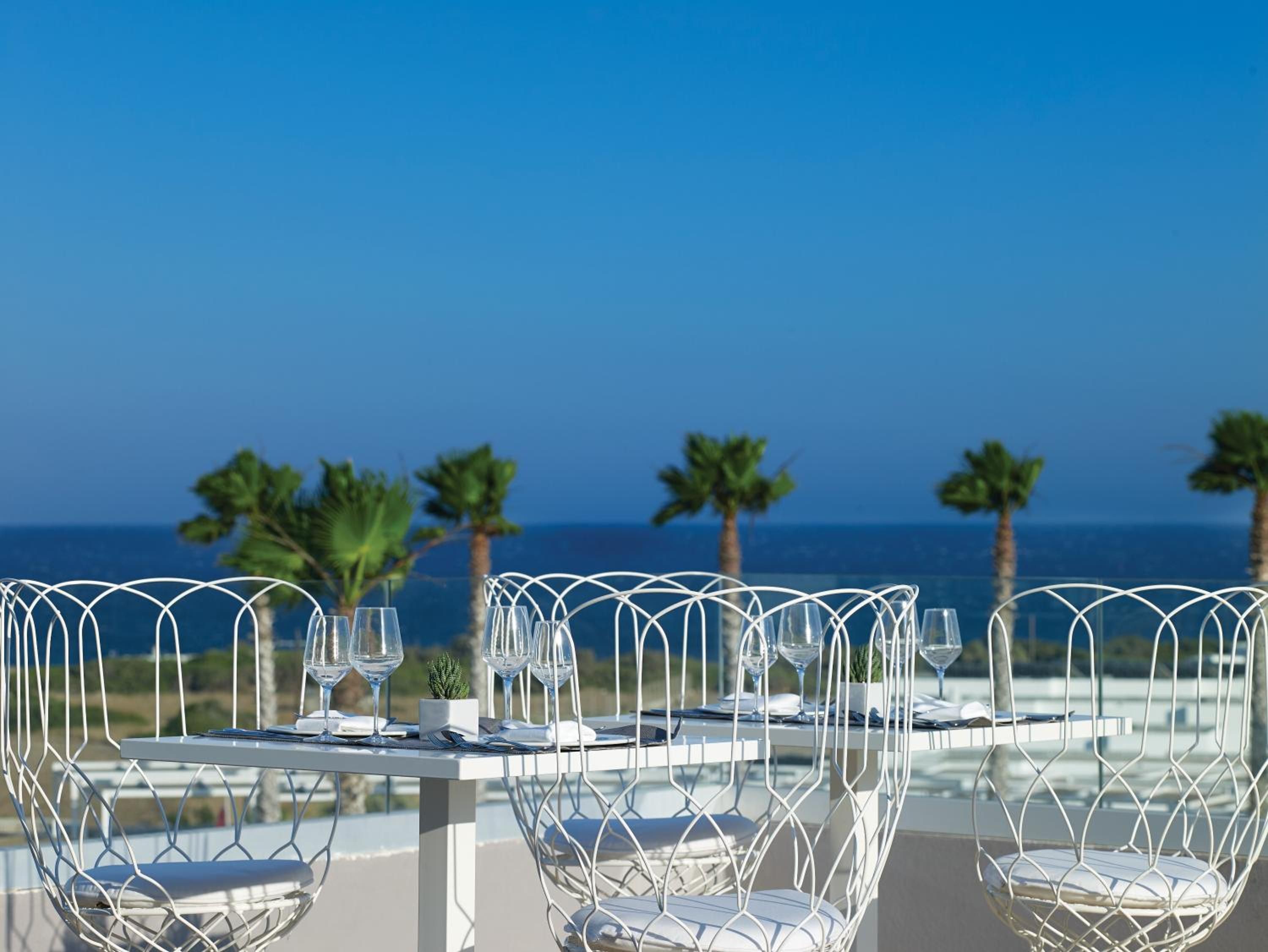A table set for dining with a view of the ocean and palm trees.
