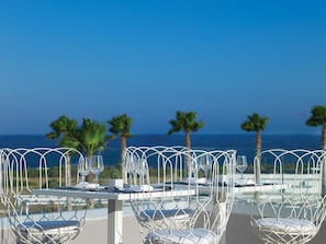 A table set for dining with a view of the ocean and palm trees.