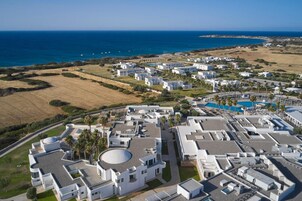 Vista aérea de un complejo turístico costero con edificios blancos modernos, una piscina y vistas al mar.