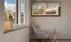 Ein Zimmer mit großem Fenster, einem Sessel, einem kleinen Tisch und einer Pendelleuchte.