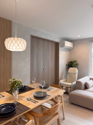 A modern dining area with a wooden table, woven chairs, a pendant light, and a sofa in the background. - sugi villa (Kitanominecho, Furano)