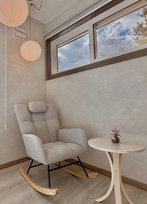 A room with a rocking chair, a small round table with a vase, a window with a view of the sky, and a wall-mounted light fixture. - sugi villa (Kitanominecho, Furano)