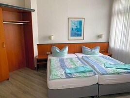 Habitación de hotel con dos camas, un armario, un cuadro en la pared y una ventana con cortinas.