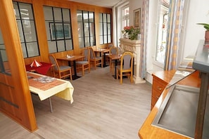 A room with wooden flooring, a dining area with tables and chairs, a kitchen area with a sink, and large windows with a view. - Hotel Birkenwerder (Birkenwerder)