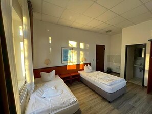 Ein Hotelzimmer mit zwei Betten, einem Schreibtisch, einem Stuhl, einem Fenster und einer Tür.