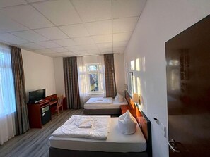 Ein Hotelzimmer mit zwei Betten, einem Schreibtisch, einem Fernseher und einem Fenster mit Vorhängen.
