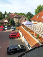 Zona residencial con coches aparcados, un edificio con tejado de tejas y un área de estar al aire libre cubierta.