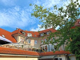 Un edificio de varios pisos con techo de tejas rojas, un balcón y un letrero que dice 'PAULANER'.