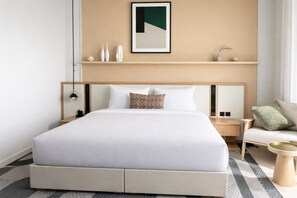 Ein modernes Hotelzimmer mit einem großen Bett, einer Kopfteil, einem Nachttisch, einer Schlaflampenablage, einem Sofa und einem Wandregal mit Dekorationen.