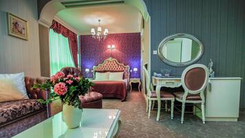 Quarto de hotel com cama, escrivaninha, cadeira, sofá, mesa de centro e um vaso com flores.
