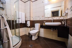 Un baño con cabina de ducha de vidrio, un inodoro, un lavamanos con espejo y un perchero para toallas.