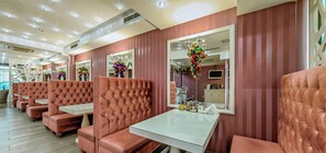 Un salón con sillones de cuero capitonados, mesas, espejos y arreglos florales decorativos.
