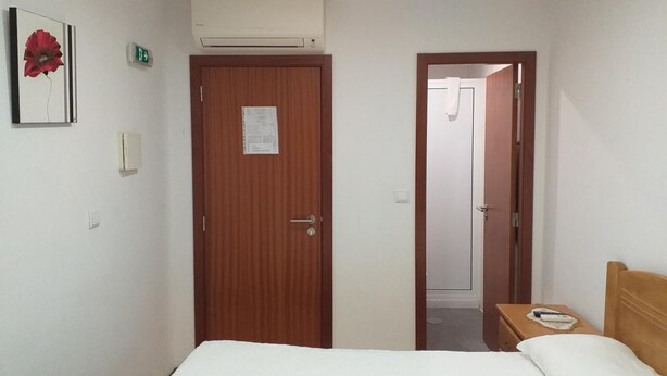 A hotel room with a bed, a wooden door, an air conditioning unit, and a small bedside table with a remote control. - Residencial Encontro (Vila Real)