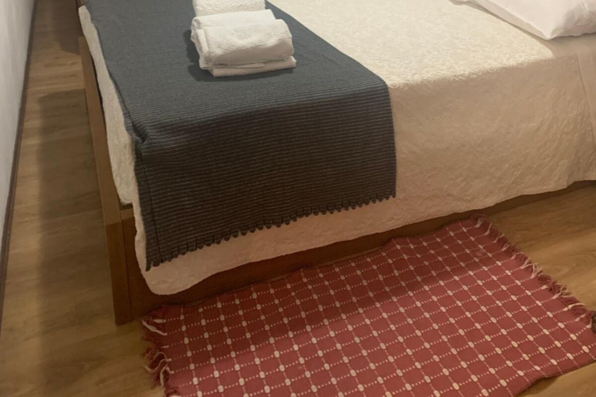 A hotel room with two beds, a desk, a chair, a TV, and a red checkered rug.