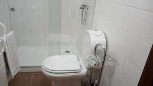 A bathroom with a toilet, a shower, and a toilet paper holder. - Residencial Encontro (Vila Real)