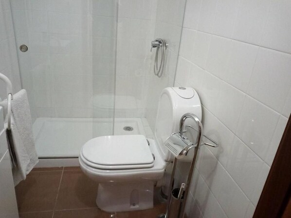 A bathroom with a toilet, a shower, and a toilet paper holder. - Residencial Encontro (Vila Real)