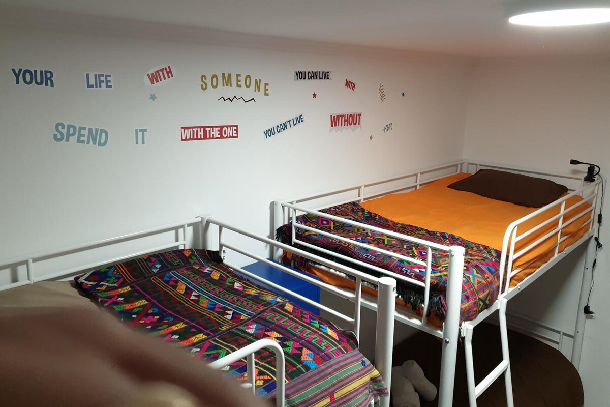 A dormitory room with bunk beds, a white wall with motivational quotes, and a ceiling light.