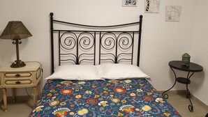 A bed with a floral-patterned bedspread, a bedside table with a lamp, and a small table with a lantern. - Lisbon Hostel Terminal 4 (Lisbon)
