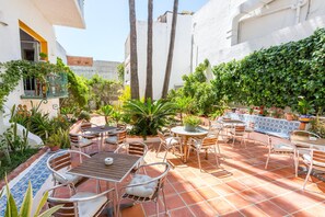 An outdoor patio with multiple seating areas, including tables and chairs, surrounded by various plants and a tiled floor. - Hotel Buigues (Teulada)