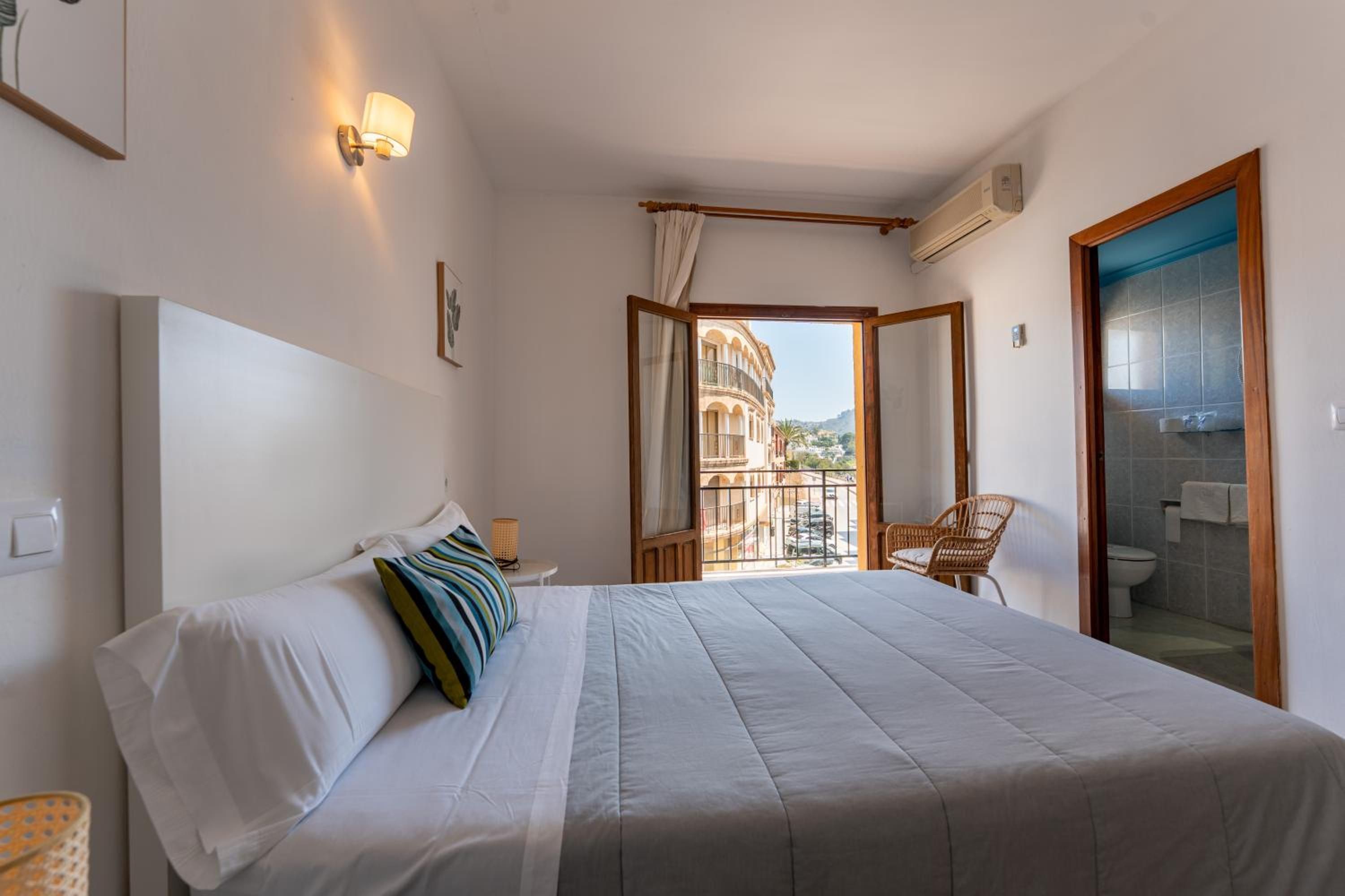 Un dormitorio con cama, una silla, un ventanal y vistas a edificios.