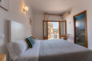 A bedroom with a bed, a chair, a window, and a view of buildings. - Hotel Buigues (Teulada)