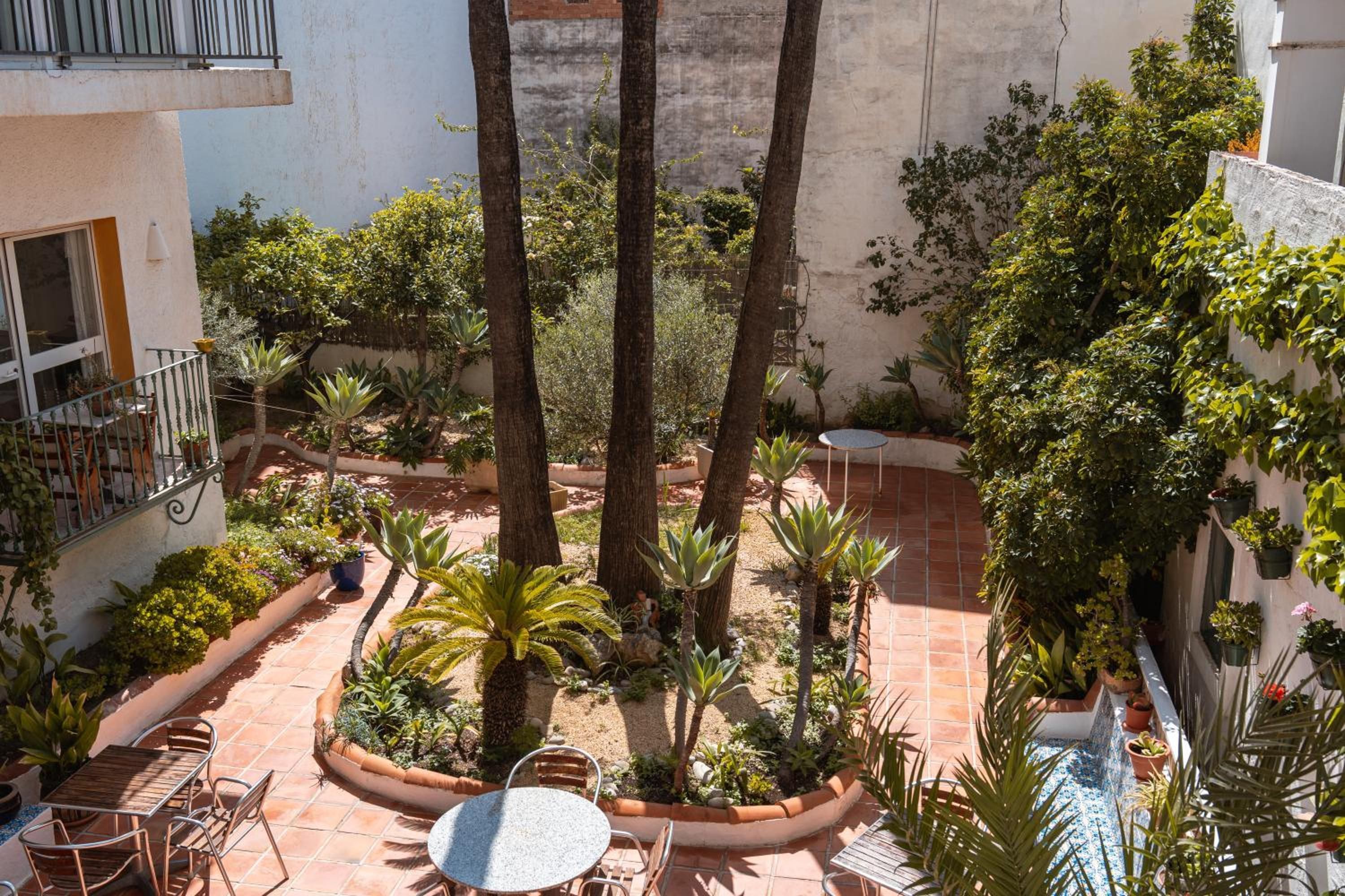 Un patio con una mesa redonda y sillas, rodeado de plantas y árboles.