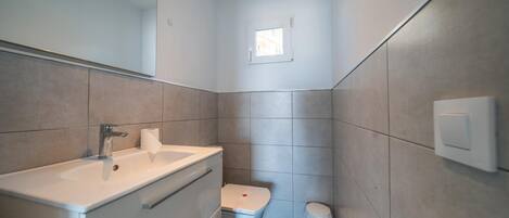 Un baño moderno con lavamanos, espejo y retrete blancos.